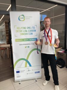 Olympic cyclist Ed Clancy in front of an Aura Innovation Centre banner holding medals